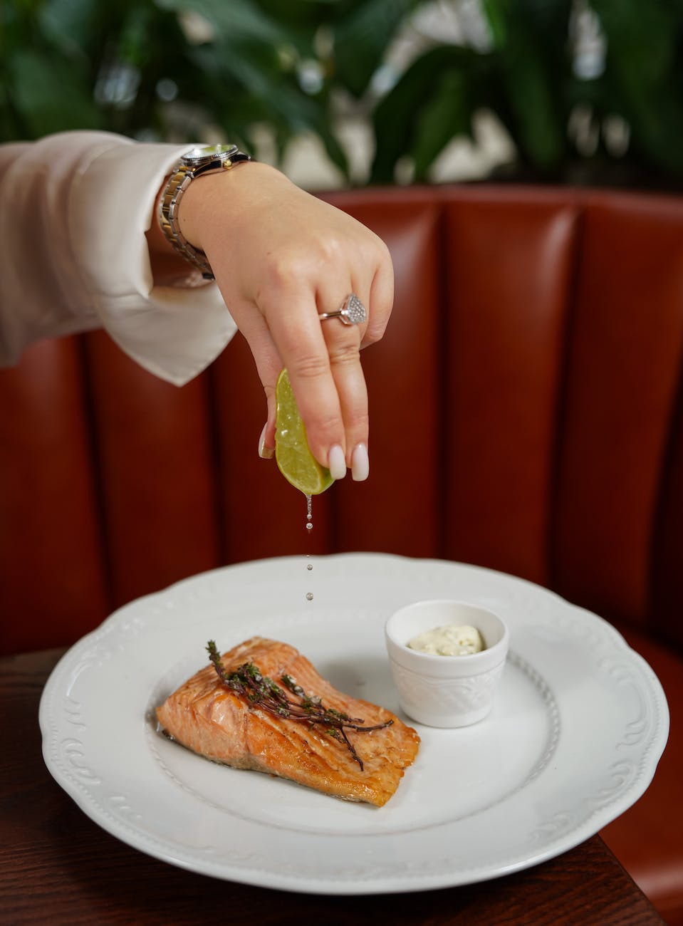 woman hand squeezing lemon over fish on plate