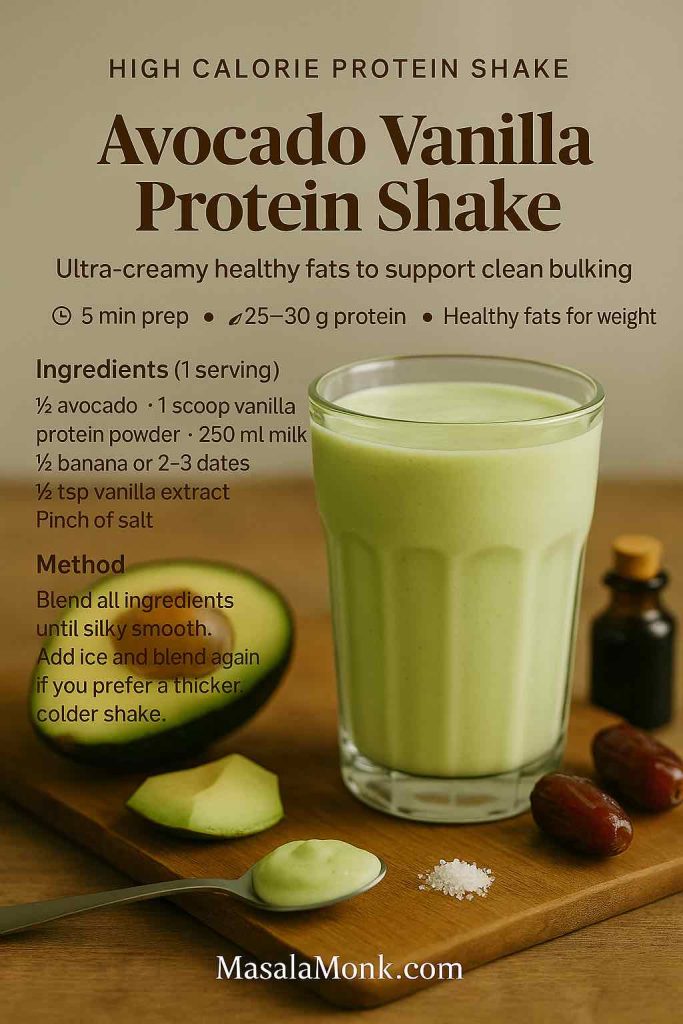 Avocado Vanilla Protein Shake high calorie protein shake recipe card with a pale green smoothie in a glass, surrounded by avocado, dates, vanilla extract and a pinch of salt on a wooden board, from MasalaMonk.com