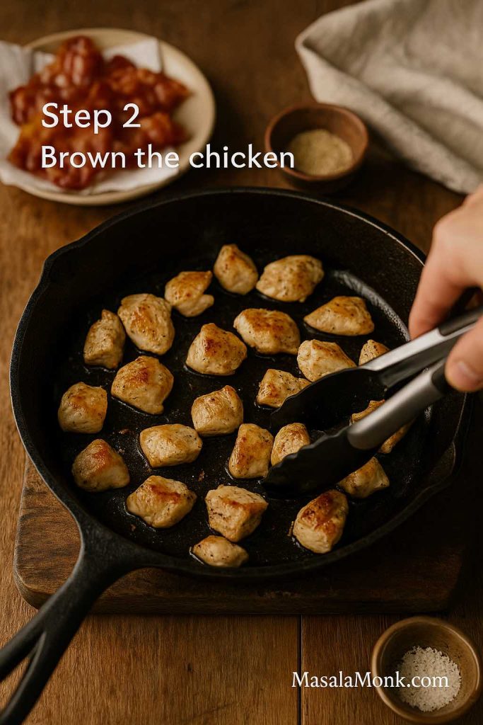 Golden-brown chicken pieces being seared in a cast iron skillet with tongs, with crisp bacon and seasoning bowls in the background for chicken bacon ranch pasta.
