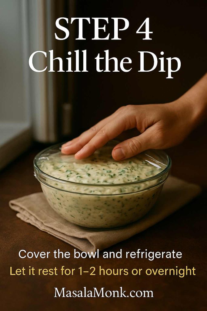 Step 4 of classic spinach dip recipe showing a hand pressing plastic wrap over a bowl of creamy spinach dip on a wooden surface before refrigerating.