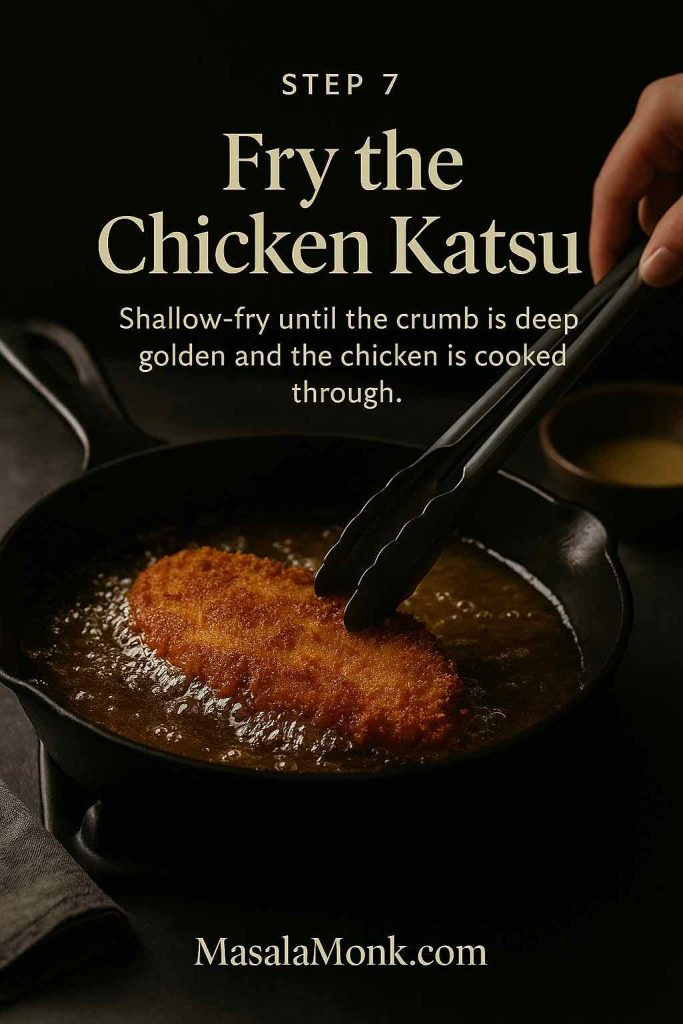Golden panko-coated chicken katsu frying in hot oil in a skillet, being turned with tongs.