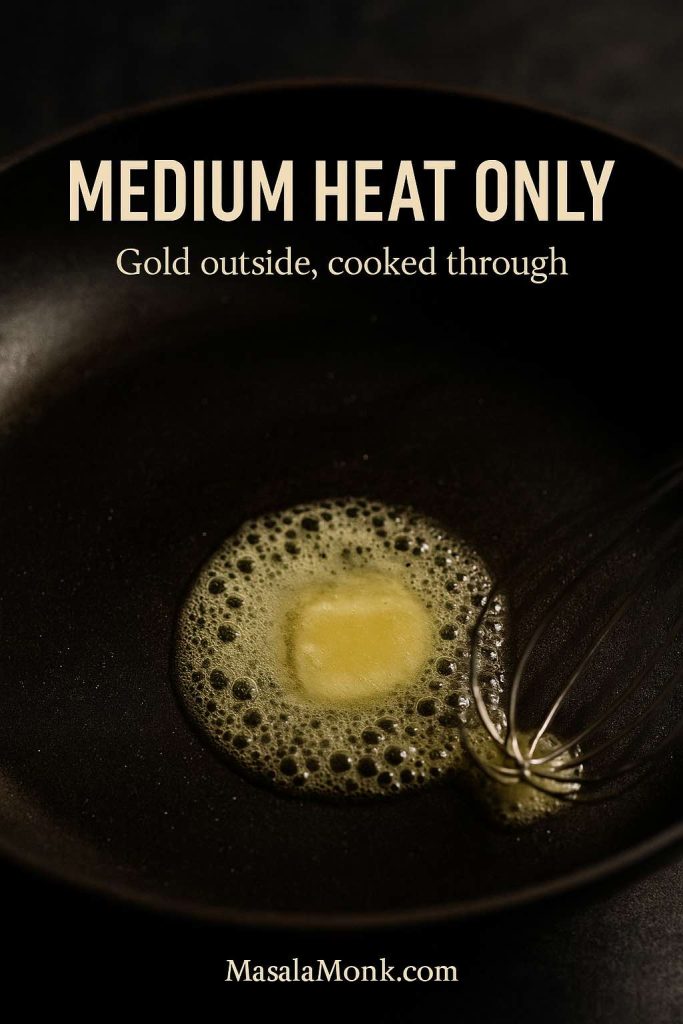 Portrait close-up of butter melting and foaming in a dark skillet for blueberry pancakes, with text overlay “Medium Heat Only” and “Gold outside, cooked through,” and MasalaMonk.com in the footer.