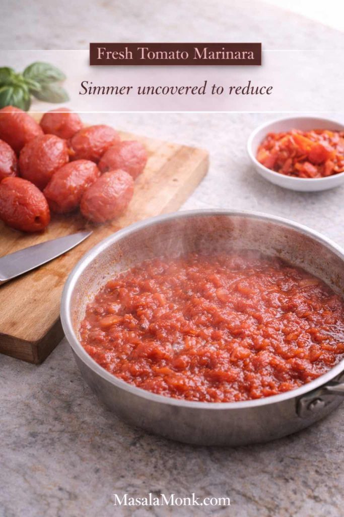 Fresh tomatoes simmering in a wide pan with peeled tomatoes on a cutting board, showing how to make marinara sauce from fresh tomatoes by reducing uncovered.