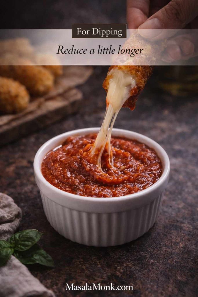 Mozzarella stick with a cheese pull dipping into a ramekin of thick marinara dipping sauce, showing a reduced marinara for dipping.