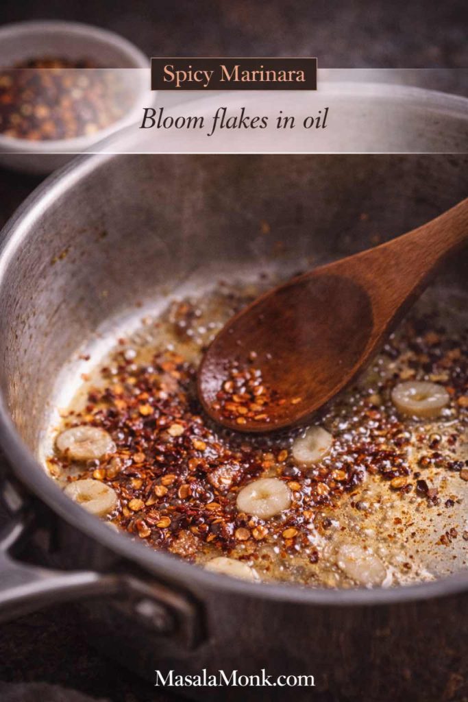 Chili flakes blooming in olive oil with sliced garlic in a saucepan, showing how to start a spicy marinara sauce before adding tomatoes.
