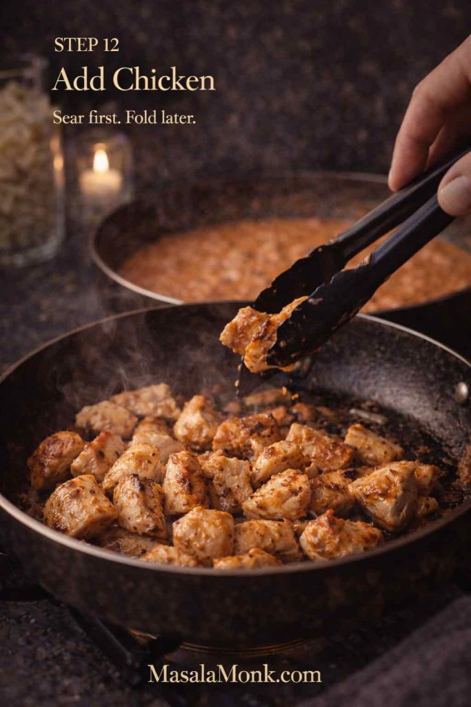 Bite-size chicken pieces searing in a skillet while tongs turn one piece, with creamy tomato vodka sauce visible in the background.