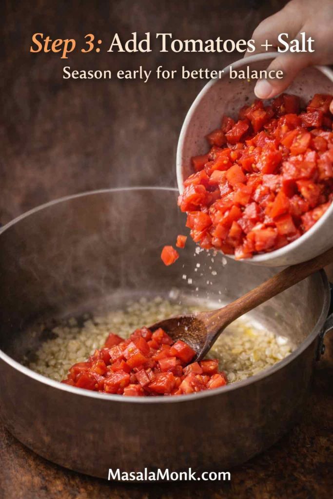 Chopped tomatoes being poured into a pot over sautéed onion and garlic while salt is sprinkled in to start tomato sauce from fresh tomatoes.