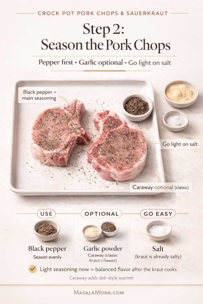 Step 2 method card for crock pot pork chops and sauerkraut showing two raw pork chops on a tray seasoned with black pepper, with optional garlic powder and caraway, and a reminder to go light on salt because sauerkraut is already salty.
