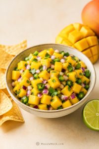 Fresh mango salsa recipe in a bowl with diced mango, red onion, jalapeño, cilantro, lime, and tortilla chips, shown chunky and glossy without tomato.