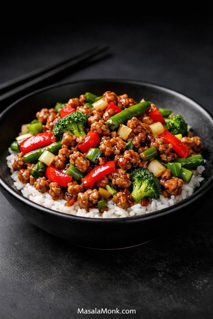 Ground pork stir fry with broccoli, green beans, red bell pepper, and rice in a black bowl.
