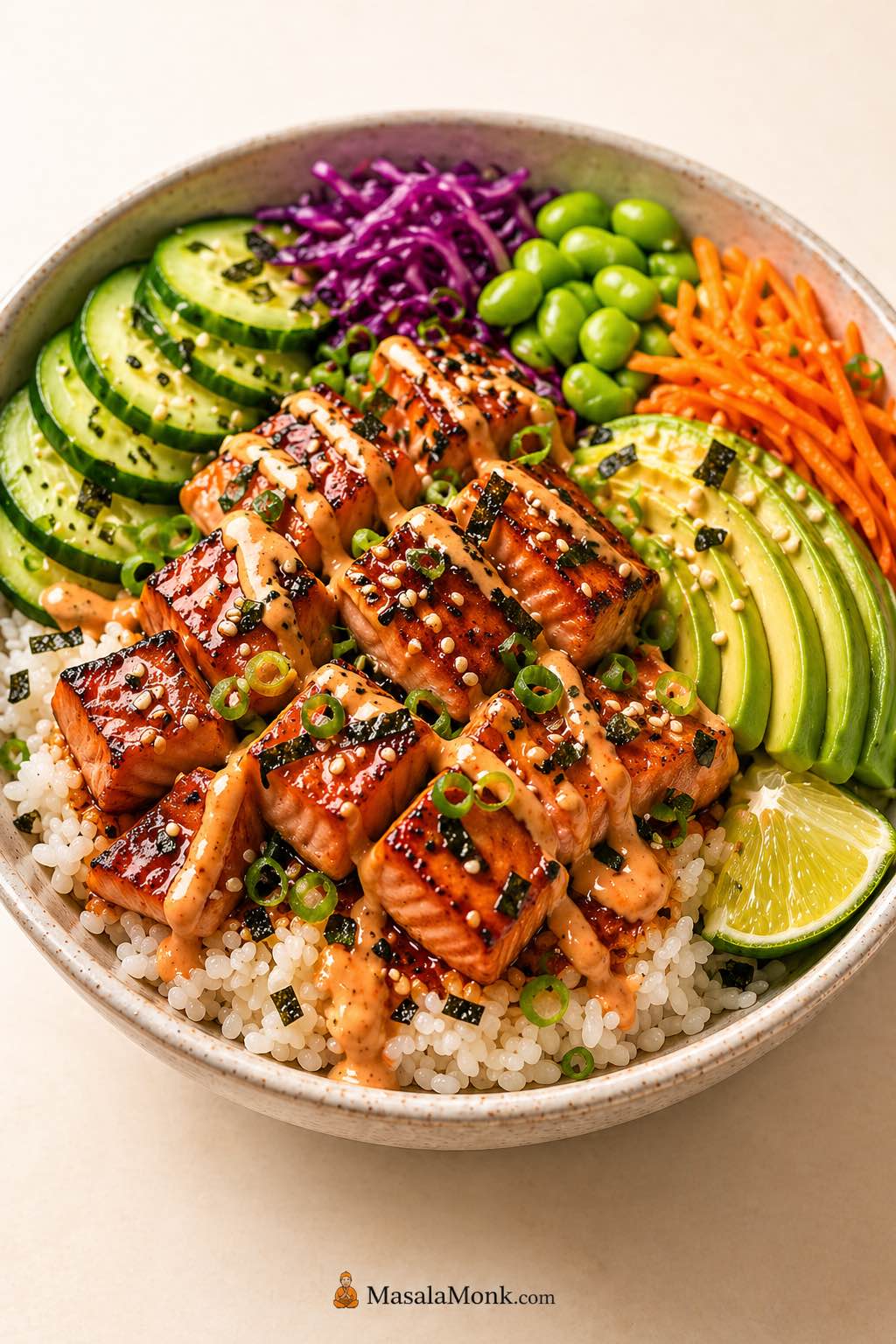 Salmon bowl recipe with pan-seared salmon bites, rice, avocado, cucumber, edamame, cabbage, carrots, sesame, scallions, lime, and creamy sauce.