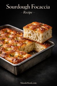 Sourdough focaccia recipe hero image showing thick golden focaccia in a metal pan with airy open crumb, deep dimples, olive oil, flaky salt, and rosemary.