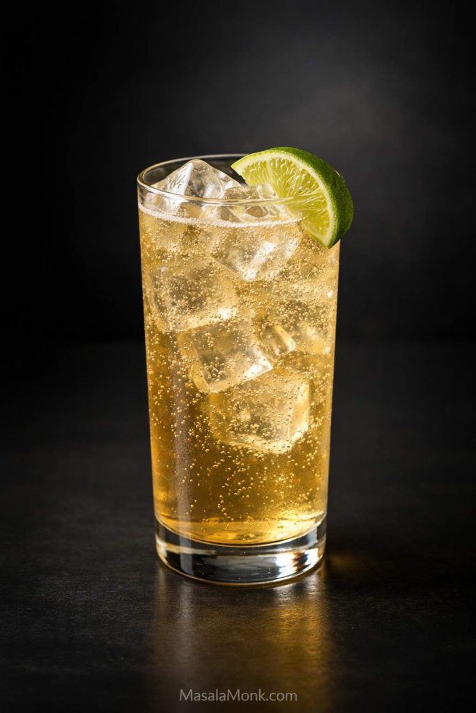 Finished whiskey ginger drink in a tall highball glass with clear ice, lively bubbles, and a lime wedge on a dark editorial background.