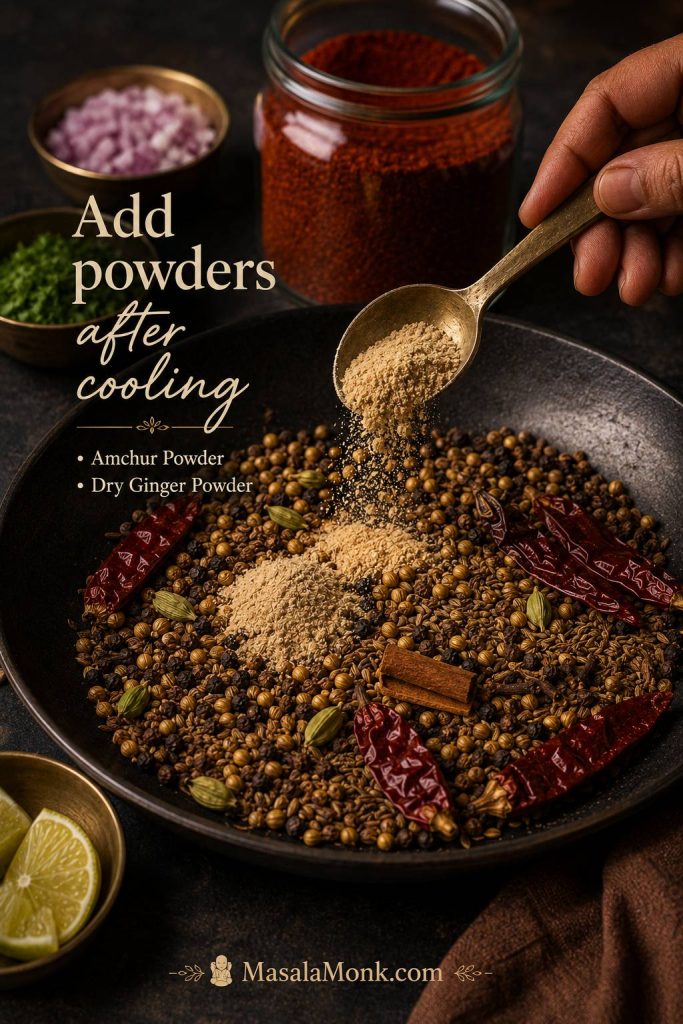 Amchur powder and dry ginger being added to cooled roasted spices before grinding pav bhaji masala.