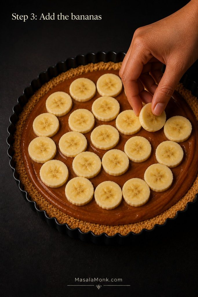 Banana slices being arranged over caramel in a biscuit crust for Step 3 of Banoffee Pie.