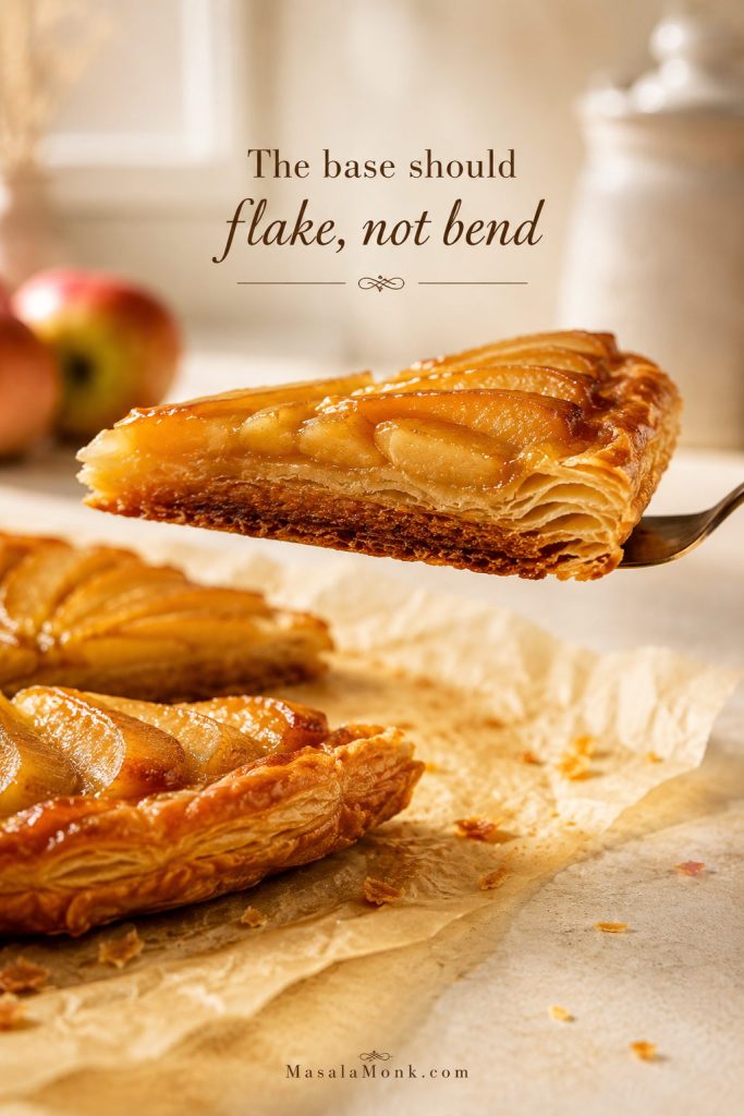 Apple tart slice lifted sideways to show a browned underside and flaky puff pastry layers.