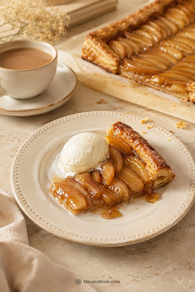 Apple tart slice served with vanilla ice cream, coffee, and the remaining tart in the background.