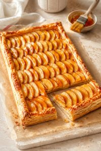 Rectangular apple tart with thin sliced apples, glossy glaze, and a golden puff pastry border on parchment.