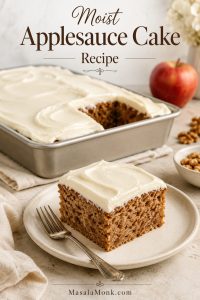 Frosted applesauce cake in a 9x13 metal pan with one square removed and plated in front, showing a soft brown crumb and cream cheese frosting.