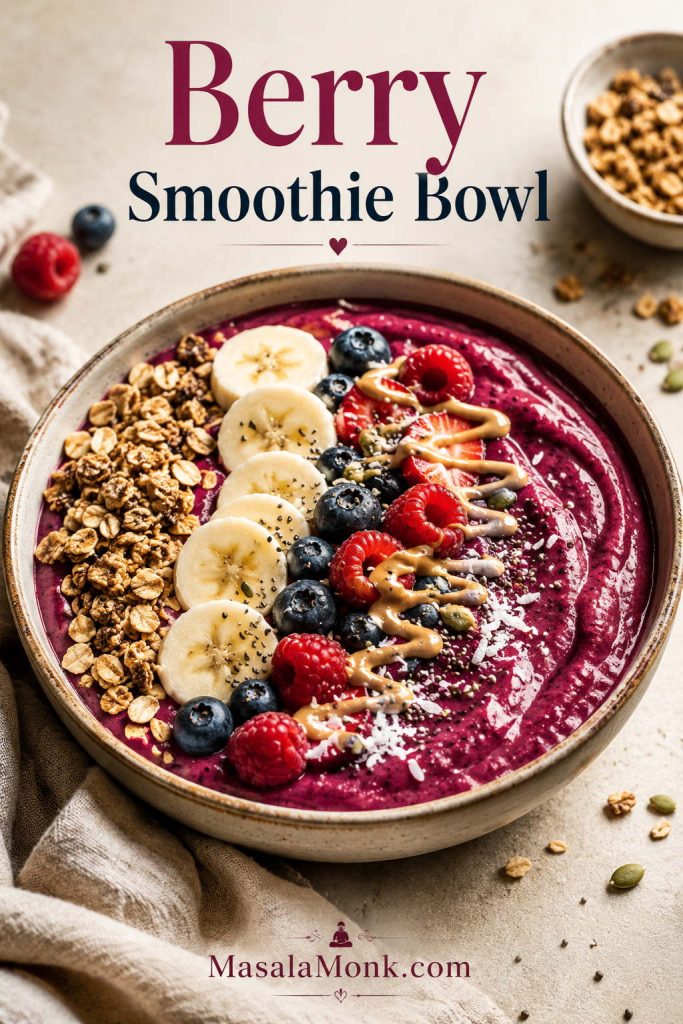 Thick berry smoothie bowl topped with granola, banana slices, berries, seeds, coconut, and nut butter drizzle.