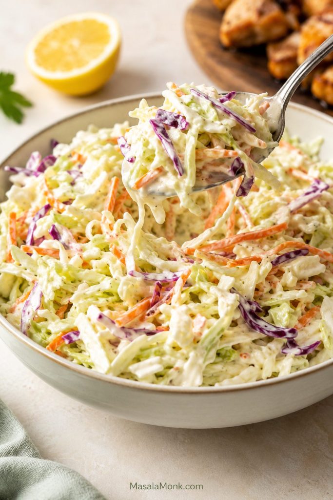 Close-up spoonful of creamy coleslaw with glossy dressing coating shredded cabbage and carrots.