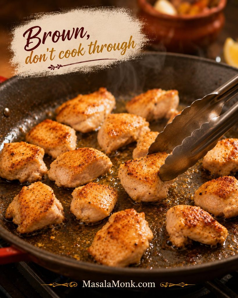 Boneless skinless chicken thigh pieces browning in olive oil with tongs in a wide skillet for paella.