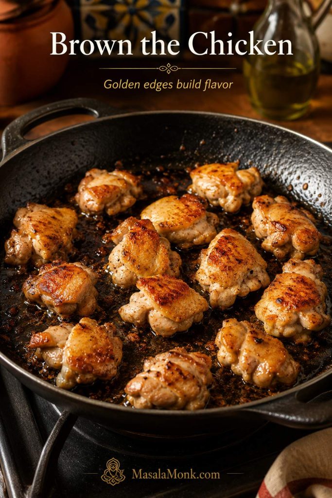 Chicken thigh pieces browning in a wide pan with golden edges and browned bits for paella.