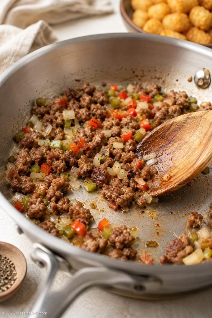 Breakfast sausage browning in a skillet with onions and peppers for tater tot breakfast casserole.