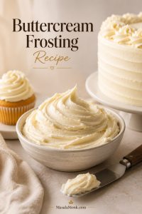 Bowl of fluffy vanilla buttercream frosting with a frosted cupcake, partial cake, and offset spatula in a warm bakery setting.