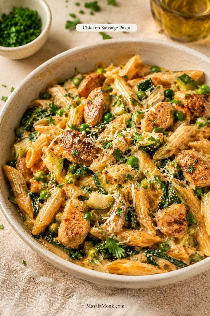 Chicken sausage pasta with penne, browned chicken sausage pieces, peas, zucchini, greens, parmesan, and a light creamy sauce.