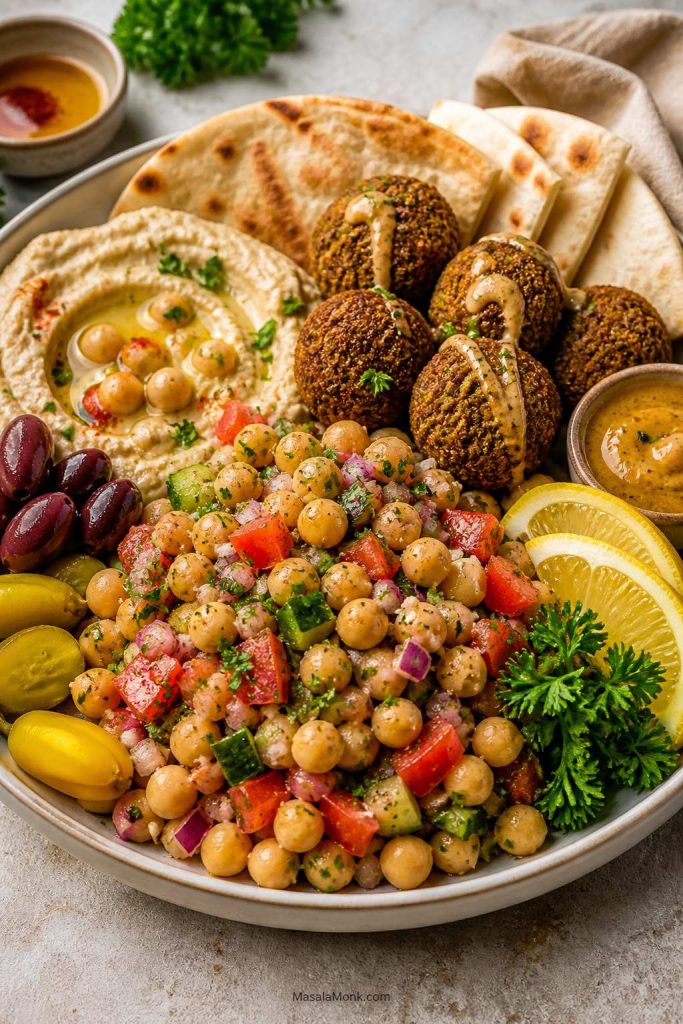 Chickpea salad served as part of a mezze plate with pita, hummus, falafel, olives, tomatoes, and lemon.