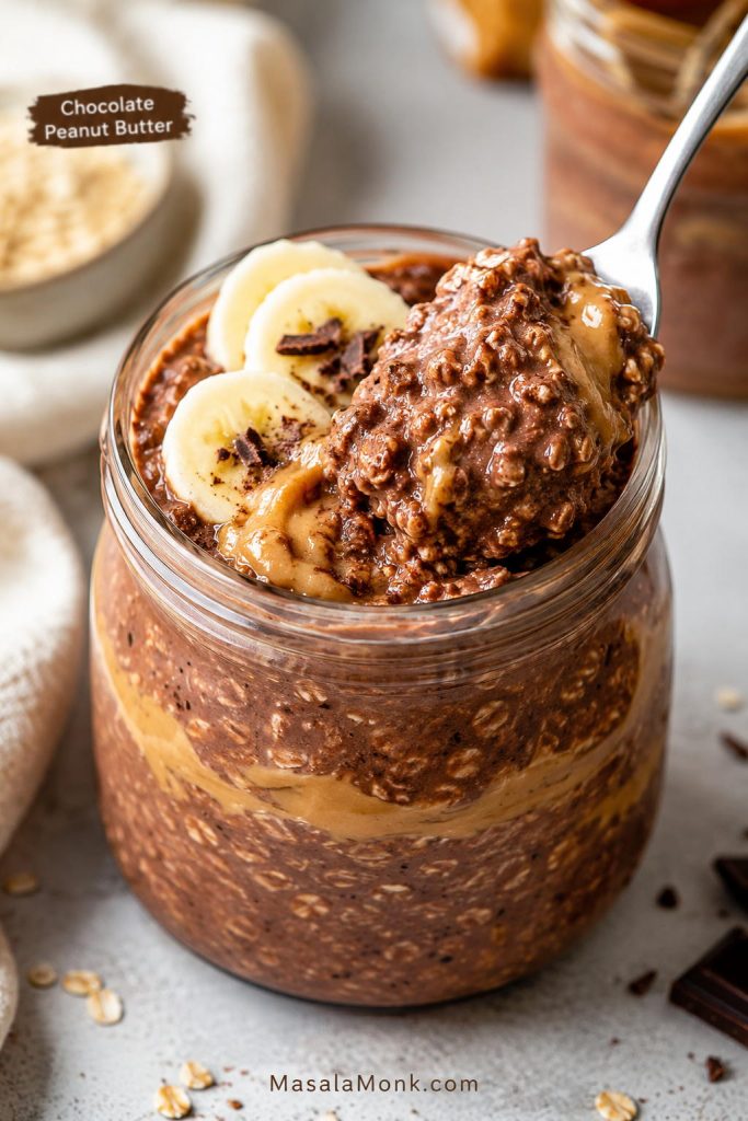 Chocolate peanut butter overnight oats with cocoa oats, peanut butter swirl, banana slices, and a spoon lifting a thick bite.