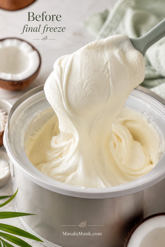 Soft churned coconut ice cream lifted with a spatula, showing a thick creamy fold before final freezing.