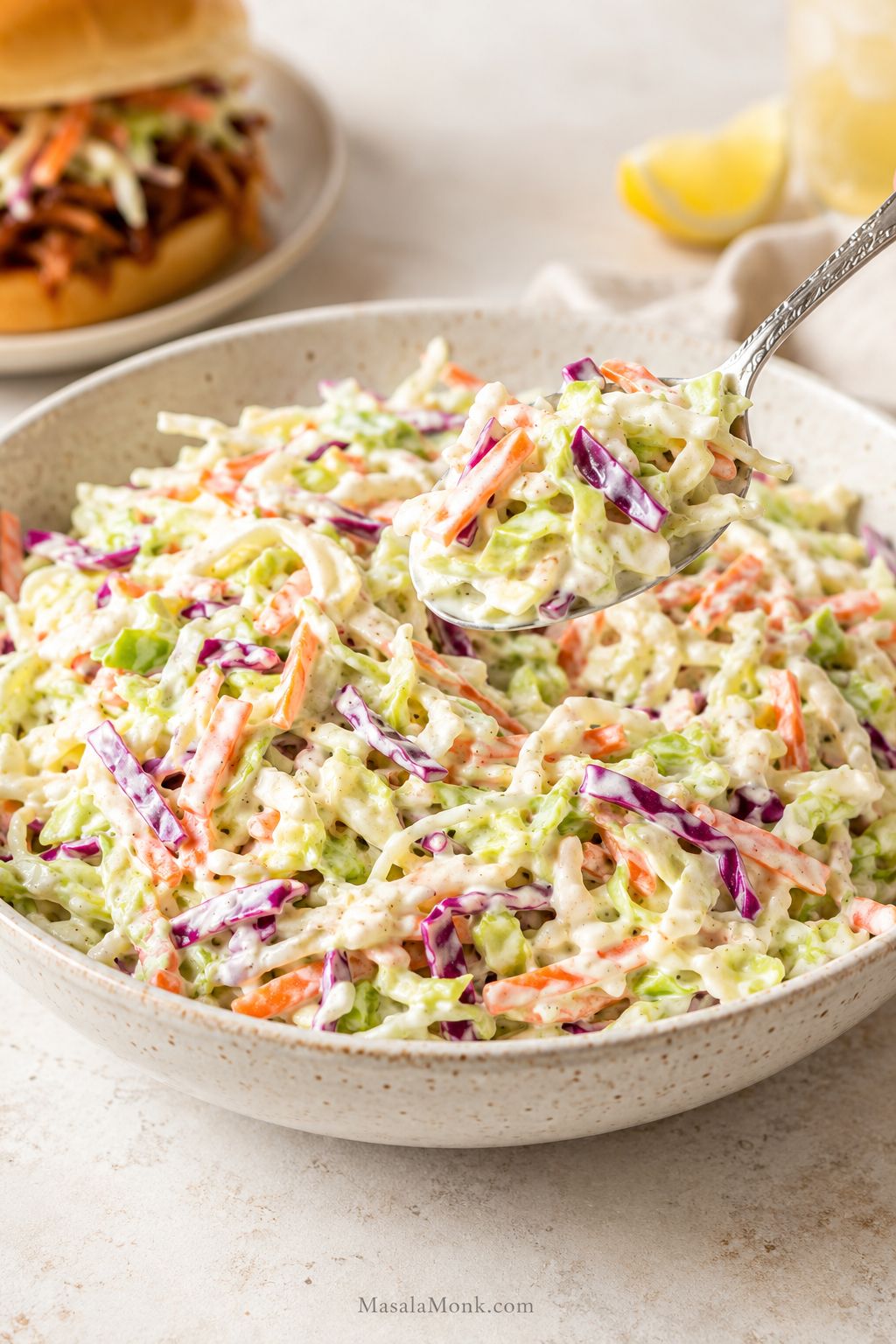 Creamy coleslaw in a bowl with shredded green cabbage, red cabbage, carrots, and a spoon lifting a serving.