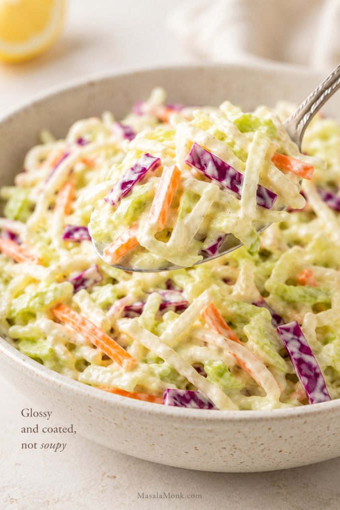 Spoonful of creamy coleslaw showing glossy dressing coating cabbage without liquid pooling in the bowl.