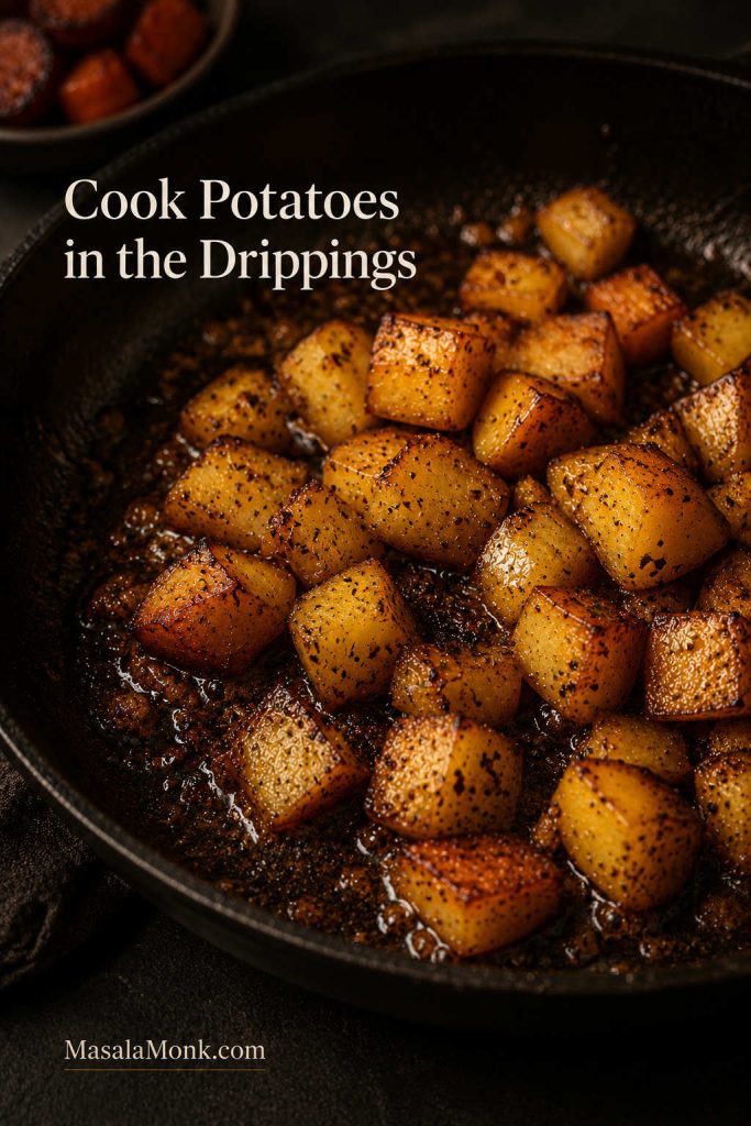 Close-up of potato cubes cooking in glossy sausage drippings with browned bits in a cast iron skillet.
