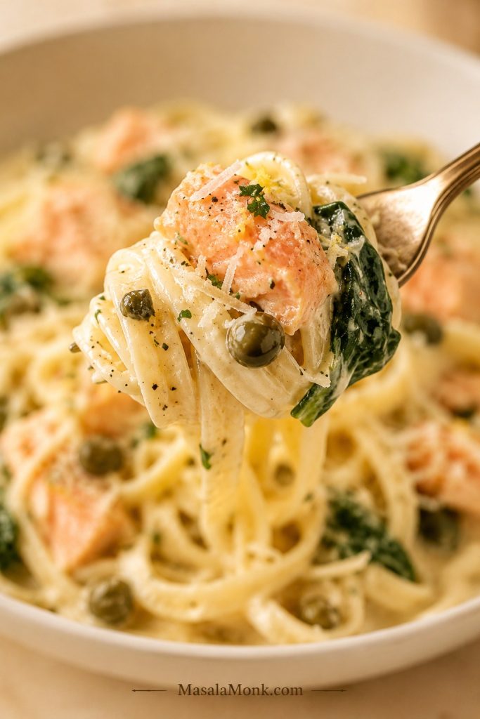 Forkful of creamy salmon pasta with pasta, salmon, spinach, capers, lemon zest, and Parmesan