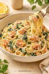 Creamy salmon pasta in a shallow bowl with salmon flakes, spinach, capers, lemon zest, Parmesan, herbs, and a fork lifting pasta.