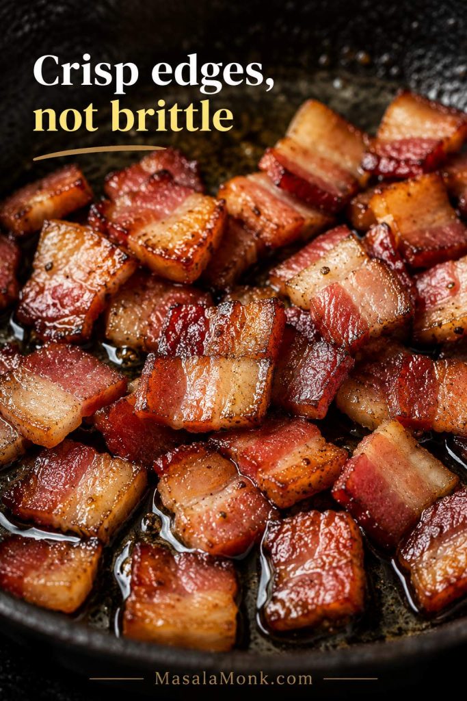 Close-up of diced bacon cooked in a skillet with crisp browned edges and rendered fat.