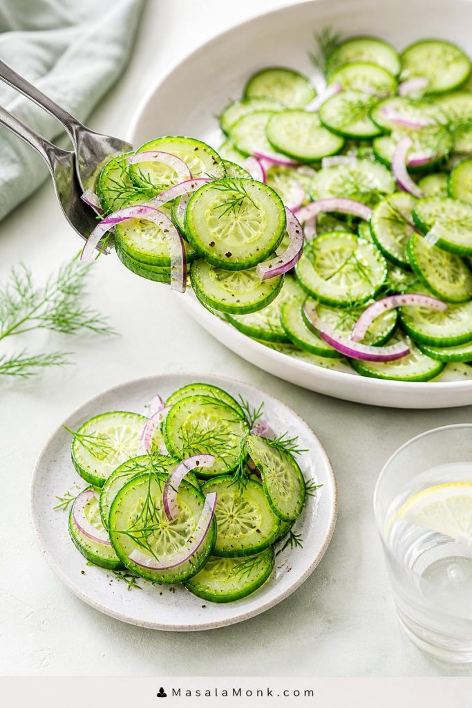 Cucumber salad being served from a large bowl onto a small plate with thin cucumber slices, red onion, dill, and a light vinegar sheen.