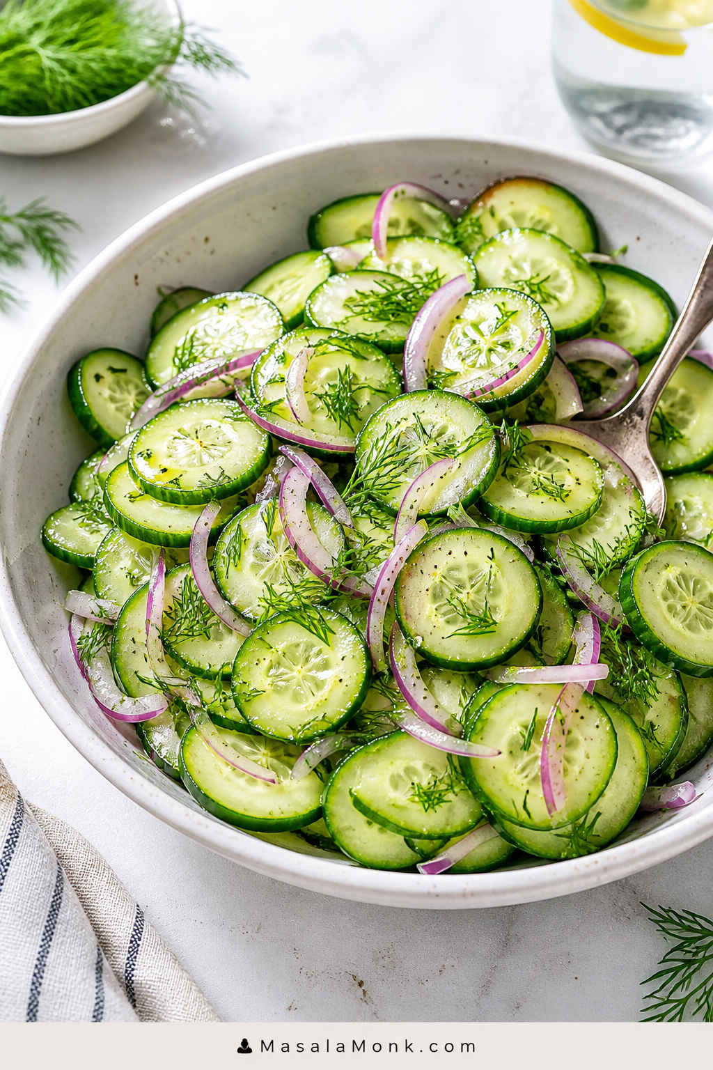 Bowl of cucumber salad with thin cucumber slices, red onion, fresh dill, black pepper, and a light vinegar dressing.
