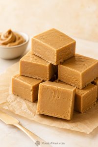 Stacked peanut butter fudge squares on parchment with smooth cut edges and a creamy interior.