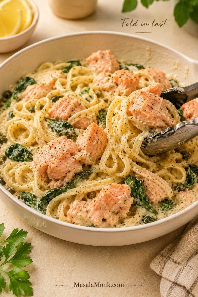 Large salmon flakes being folded into creamy pasta with spinach and sauce