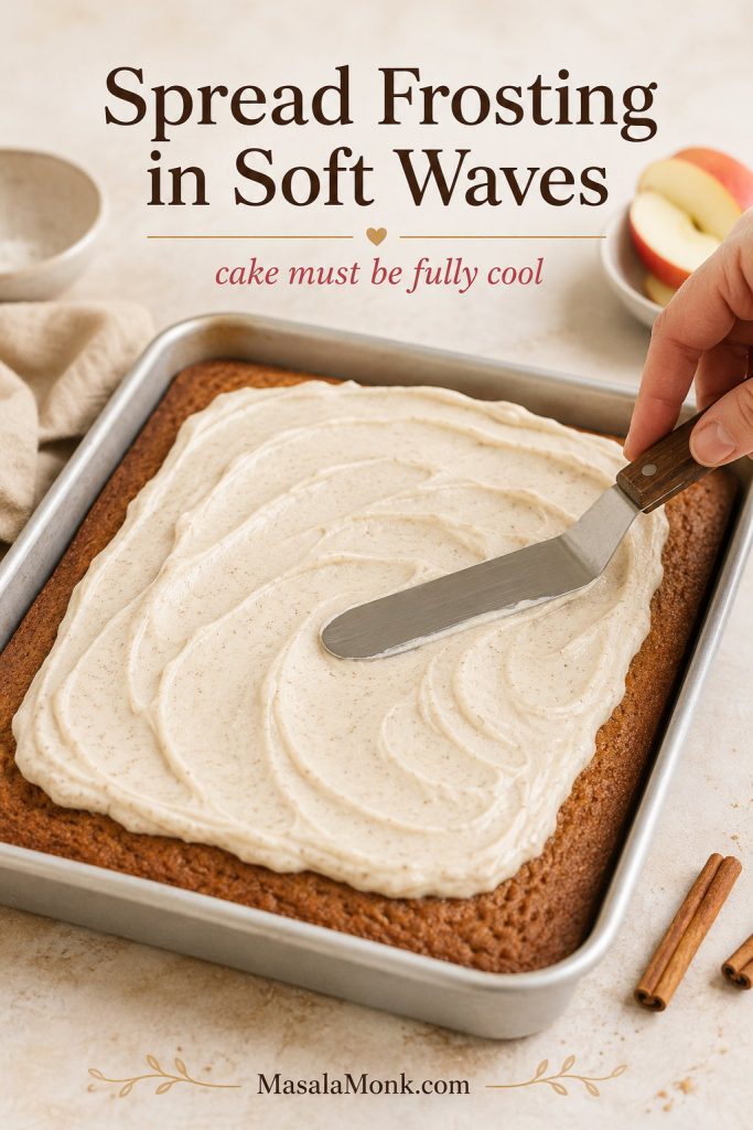 Cream cheese frosting being spread in soft waves over a cooled 9x13 applesauce cake with an offset spatula.
