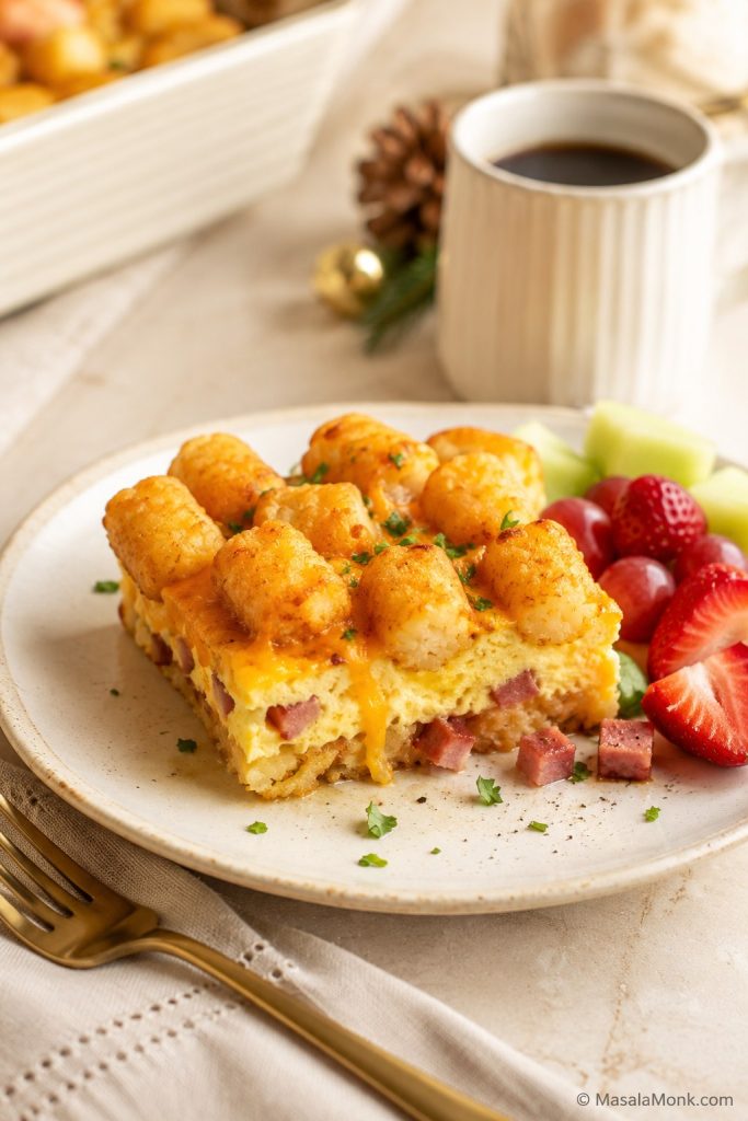 Ham and cheese tater tot breakfast casserole served with fruit, showing diced ham, eggs, cheese, and golden tots.