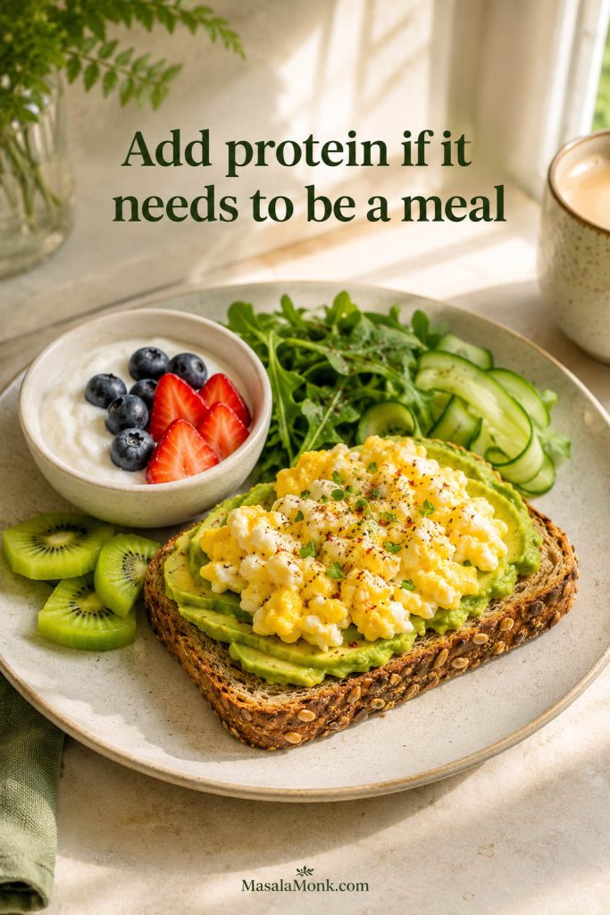 High-protein avocado toast breakfast with seeded toast, avocado, scrambled egg, yogurt with berries, greens, cucumber, and kiwi.