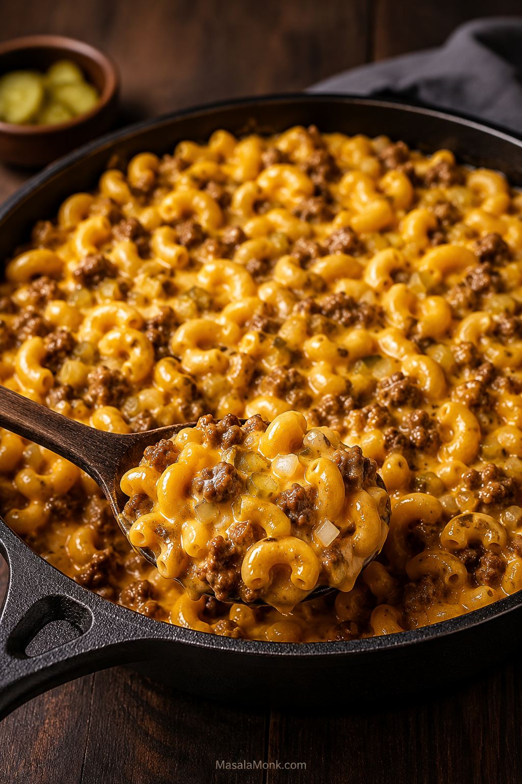 Homemade cheeseburger macaroni in a dark skillet with elbow pasta, browned ground beef, glossy cheddar sauce, and a serving spoon.