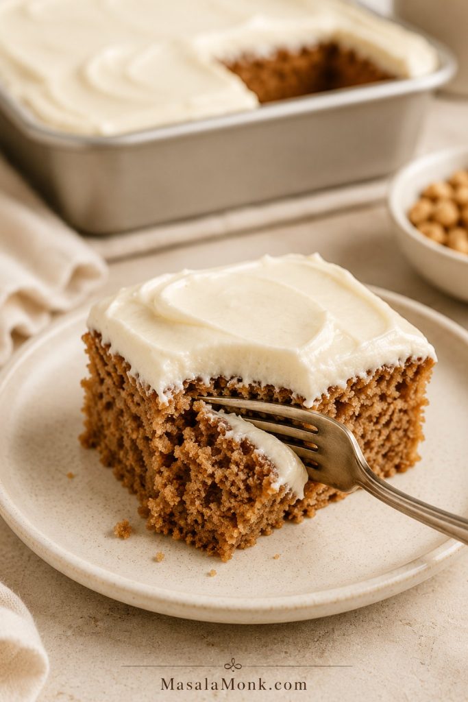 Close-up of a frosted applesauce cake square on a cream plate with a fork pressing into the soft crumb.