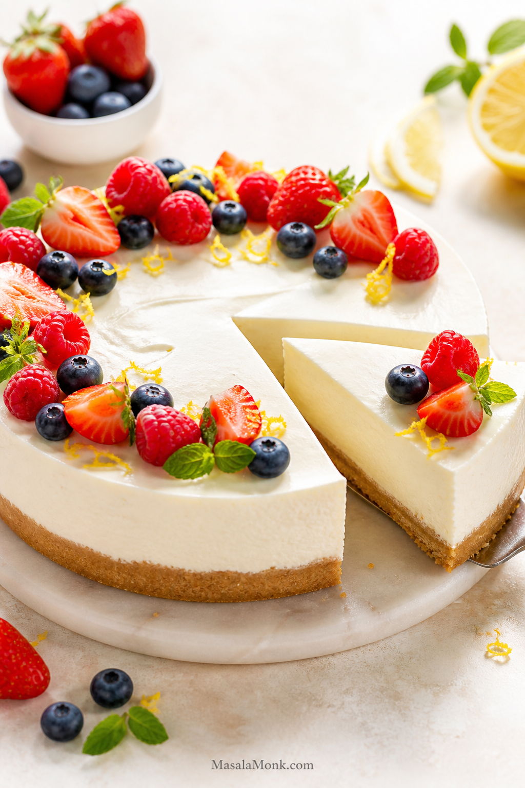 Finished no-bake cheesecake with one slice removed, creamy white filling, golden crumb crust, berries, and lemon zest