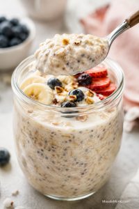 Creamy overnight oats in a glass jar with fresh fruit, nuts, and a spoon lifting a thick bite.